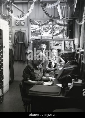 1953, historische, weibliche Angestellte, die in einem kleinen Büro bei der Hepworths Bekleidungsfirma, Leeds, England, Großbritannien, arbeiten. An der Wand sind Ammer- und Union-Jacks, mit einem Bild von Königin Elizabeth II. Und Prinz Philip - in einem Kilt - mit zwei kleinen Jungen. Die Fahne und die Fahne feiern die Krönung der Königin auf den britischen Thron. Die Providence Works auf Clay Pit Lane war die Heimat von Joseph Hepworth und Son, ein Bekleidungsunternehmen begann im Jahr 1865 und die bis 1905 hatte 143 Geschäfte. Später im Jahrhundert, Hepworths wurde Next. Stockfoto