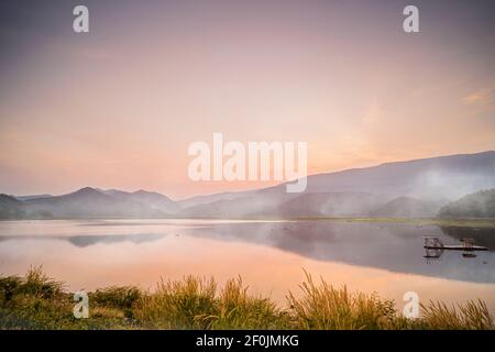 Idyllisch dramatischer Sonnenuntergang mit der Szene von Nebel über den Lake Mountains im Hintergrund am Khao Luang Reservoir. In Sukhothai Thailand Stockfoto