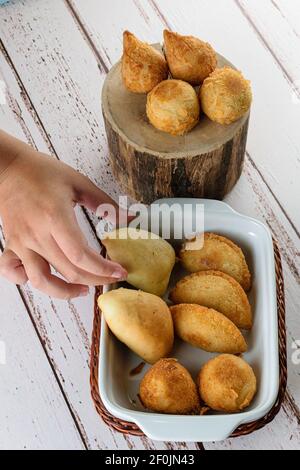 Gebratene und geröstete brasilianische Savorys. Die Hand der Frau nimmt einen der Bohnenkraut. Stockfoto