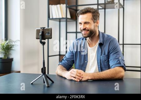 Lächelnd reif schöner Mann blogger, stilvoll, sitzt vor dem Handy auf Stativ Stabilisator Aufnahme Streaming-Video, teilen Einkaufserlebnis, empfehlen oder bewerten Service online Stockfoto