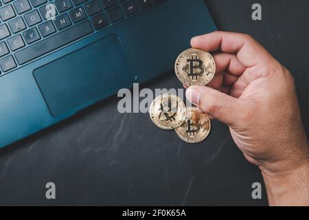 Geschäftsmann hält Bitcoin und Laptop auf schwarzem Hintergrund. Elektronisches virtuelles Geld für Web-Banking und internationale Netzwerk-Zahlung, Currency Techn Stockfoto