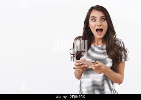 Aufgeregt, glücklich und fröhlich kaukasischen weiblichen Sieg im Spiel, Pass-Level, schlagen Gegner im Kampf mobile online, halten Smartphone horizontal Stockfoto
