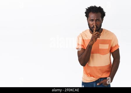 Shhh Stille in der Klasse. Seriös aussehende afroamerikanische bärtige Kerl in gestreiften T-Shirt fordern ruhig, shushing, drücken Sie Zeigefinger zu verschlossenen Lippen und Stockfoto