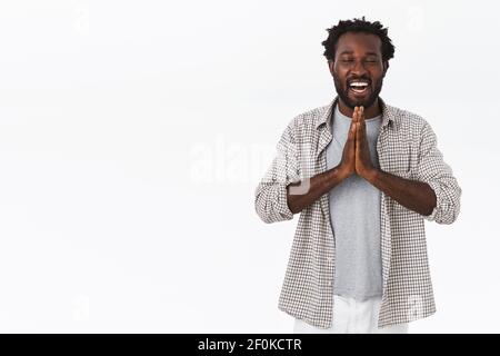 Entspannter und friedlicher fröhlicher afroamerikanischer bärtiger Mann mit Afro-Frisur, Wunsch machend oder Namaste sagend, mit zusammengeklemmten Händen betend Stockfoto