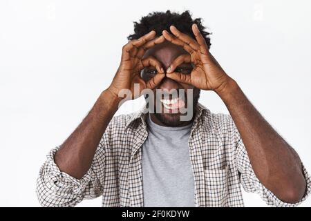 Sorglos, gut aussehend verspielt lustig afroamerikanischen Mann mit Bart, macht goofy Ausdruck, zeigt Brille mit okay Zeichen, Kreise über Augen, Stick Stockfoto