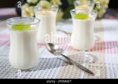 Italienische Dessert Panna Cotta in kleinen transparenten Gläsern mit Trauben und Banane auf einer karierten Tischdecke dekoriert. Stockfoto