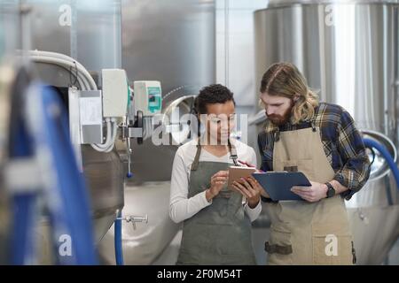 Waist-up-Porträt von zwei jungen Arbeitern mit digitalen Tablet bei der Inspektion der Produktion in modernen Craft Brauerei, Copy Space Stockfoto