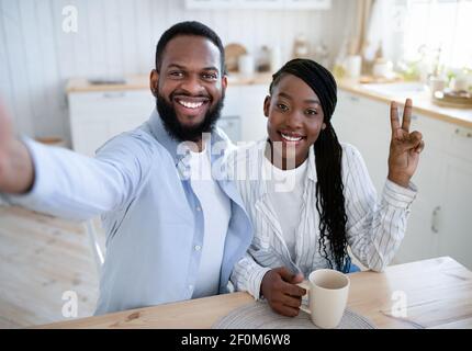 Fröhliche Schwarze Ehegatten Nehmen Selfie Beim Trinken Morgenkaffee In Küche Zusammen Stockfoto