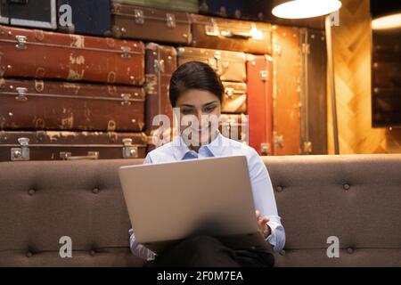 Lächelnde indische Frau mit Laptop, sitzt auf der Couch im Büro Stockfoto