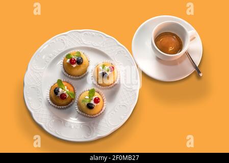 tasse Espresso Kaffee mit Muffins in weißen Teller in Ansicht von oben isoliert auf orangefarbenem Hintergrund Stockfoto