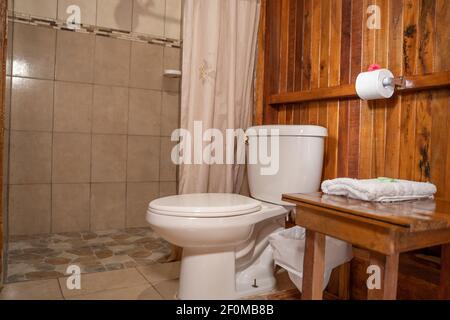 Rustikales Hotelbadezimmer mit Holzmöbeln mit einem gefalteten Handtuch und einer Dusche daneben mit einem weißen Vorhang. Stockfoto