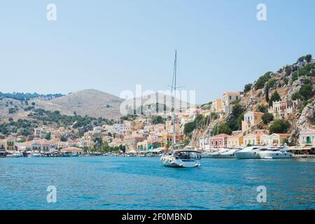 Yatch bei Ankunft am Hafen von Symi. Blick auf das bunte Dorf an einem Sommertag. Dodekanes, Griechenland Stockfoto