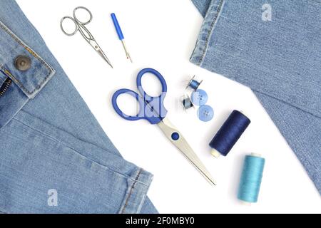 Tailor's Accessoires zum Nähen mit Jeans, Schere und Spule aus blauen Fäden, isoliert auf weißem Hintergrund Stockfoto