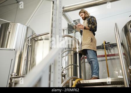 Ganzkörperportrait des bärtigen Braumeisters, der die Produktion in der Bierfabrik kontrolliert, Kopierraum Stockfoto