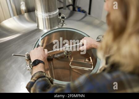 Nahaufnahme eines männlichen Arbeiters, der Tanks in der Brauerei öffnet, Bierherstellung, Kopierraum Stockfoto