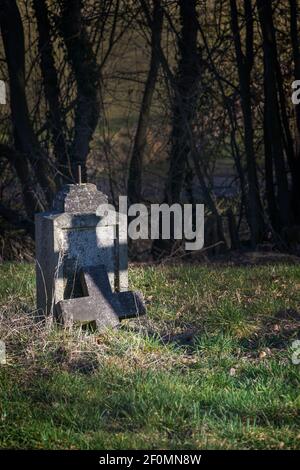 Alte Grabsteine mit gebrochenem Kreuz, aber mit einem Schatten in Kreuzform unter Bäumen auf einem verlassenen Friedhof, religiöses Symbol, Kopierraum, ausgewählter Fokus Stockfoto