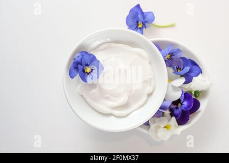 Natürliche kosmetische Salbe und Viola oder violette Blumen in weißen Schalen auf hellgrauem Hintergrund, Kopierraum, Hochwinkel Ansicht von oben, ausgewählte Focu Stockfoto
