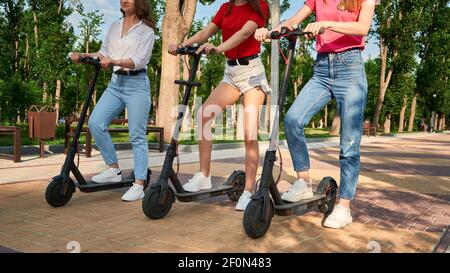 Drei junge Freundinnen auf den Elektro-Scootern Spaß in der Stadt Straße im Sommer sonnigen Tag. Outdoor-Porträt von drei Freunden Mädchen Reiten elektrisch Stockfoto