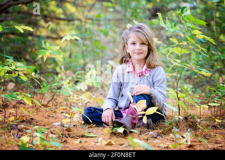 Junge blonde Mädchen sitzt auf dem Boden im Wald. Stockfoto