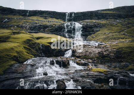 Wasserfälle in der Ortschaft Saksun auf den Färöer Inseln. Keine Menschen um, traditionelle Häuser aus Stein. Stockfoto