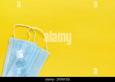 Coronavirus Schutzkonzept flach legen. Einwegmasken und Desinfektionsmittel auf gelbem Hintergrund mit Platz für Text. Stockfoto
