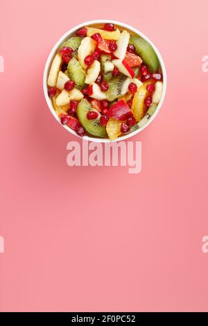 Schüssel mit Obstsalat auf rosa Hintergrund. Saftige und reife Fruchtscheiben. Draufsicht Stockfoto