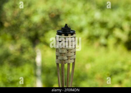 Eine Gartenfackel, die im Garten steht. Im Hintergrund Grün aus verschiedenen Pflanzen und Sträuchern. Stockfoto