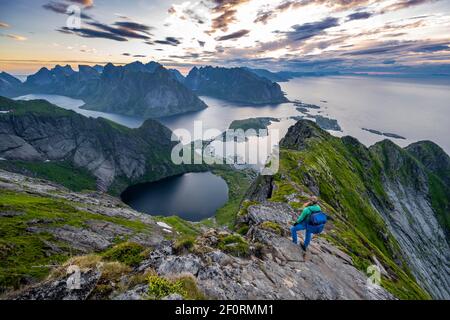 Abendstimmung, junger Wanderer auf dem Grat genießt den Blick von Reinebringen, Reinebriggen, Hamnoy, reine und dem Reinefjord mit Bergen Stockfoto