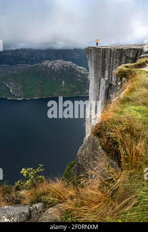 Person steht auf steilen Felsen, Preikestolen Felsspire, Lysefjord, Ryfylke, Rogaland, Norwegen Stockfoto