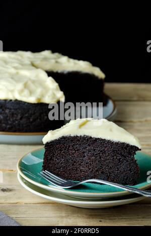 Eine Scheibe oder Servierplatte von Guinness und Schokoladenkuchen auf einem Beilagenteller. Der Hauptkuchen ist im Hintergrund dargestellt Stockfoto