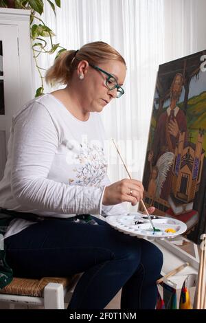 Frau in ihrem Wohnzimmer, die Öl bemalt und ein Bild malt Auf einer Staffelei, die ihr Hobby genießt Stockfoto