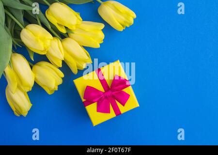 Geschenk mit rosa Schleife und gelben Tulpen auf dem blauen Hintergrund. Draufsicht. Speicherplatz kopieren. Stockfoto