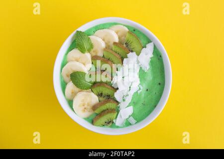 Smoothies Schale mit Banane, Kiwi und Kokosnusschips in der Mitte des gelben Hintergrunds.Draufsicht.Platz kopieren. Stockfoto
