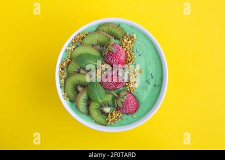 Smoothies Schüssel mit Banane, Kiwi, gefrorene Erdbeere und Bienenpollenon in der Mitte des gelben Hintergrunds.Draufsicht.Copy Space.Closeup. Stockfoto
