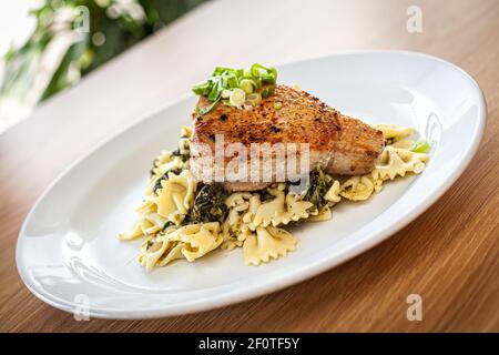 Gekochte Speisen auf einem weißen Teller - Thunfisch auf Spinatpasta serviert. Stockfoto