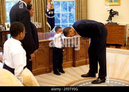 Präsident Barack Obama beugt sich, so dass der Sohn eines Mitarbeiters des Weißen Hauses während eines Besuchs im Oval Office im Mai 8 2009 seinen Kopf klopfen kann. Stockfoto