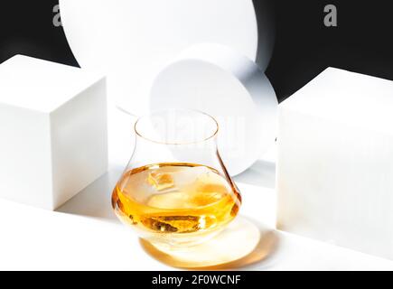 Zeitgenössisches Stillleben mit Whiskey, Scotch oder Bourbon in Glas mit Scherbeneis auf schwarzem weißem Hintergrund mit geometrischen Kuben und Kreisen Stockfoto