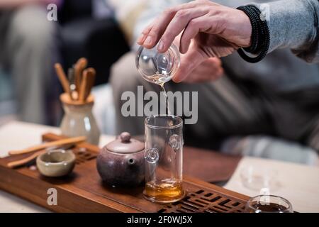 Nahaufnahme eines traditionellen orientalischen Teerituals. Ein Mann gießt schwarzen reifen Tee aus einer Flasche in eine Probierschale. Verschwommener Hintergrund. Stockfoto