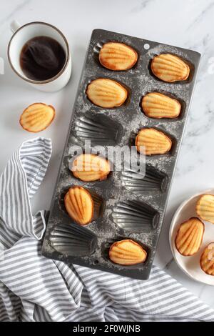 Blick von oben auf frisch gebackene madeleine-Kuchen mit einem Dampfende Tasse Kaffee auf weißem Marmor Hintergrund Stockfoto