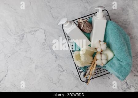 Set von Duschzubehör in einem Korb auf einem Marmorboden. Enthält Flaschen von Kosmetika, Loofa, Zahnbürsten, Handtuch. DIY Öko-Kosmetik. Konzept z Stockfoto