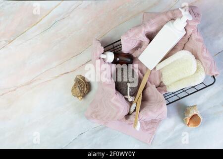Set von Duschzubehör in einem Korb auf einem Marmorboden. Enthält Flaschen von Kosmetika, Loofa, Zahnbürsten, Handtuch. DIY Öko-Kosmetik. Konzept z Stockfoto