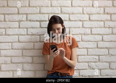 Lachende junge Frau, die Spaß mit Zelle nahe Ziegelwand hat Stockfoto