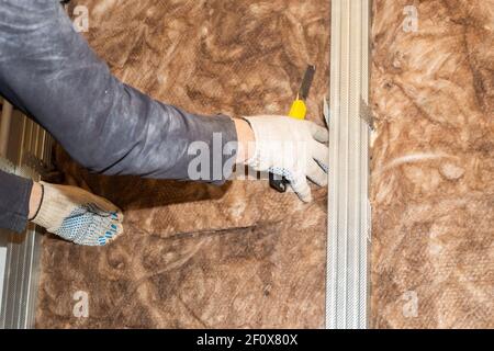 Der Arbeiter fügt Mineralwolle an die Wände für weitere Gipskartonverkleidungen. Wärmedämmung und Schalldämmung des Gehäuses. Renovierung des Hauses. Stockfoto