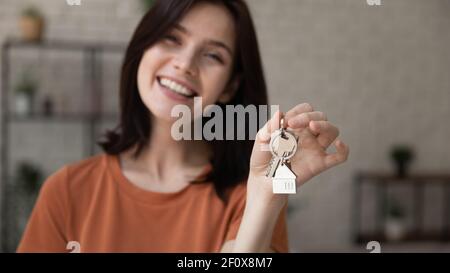 Glückliche Frau, die auf die Kamera schaut und den Schlüssel aus dem neuen Haus zeigt Stockfoto