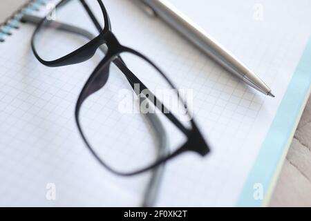 Schwarze Brillen, Stift und Notizbuch liegen auf dem Tisch Stockfoto