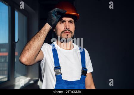 Bärtiger Ingenieur in Overalls setzt einen Helm auf Stockfoto