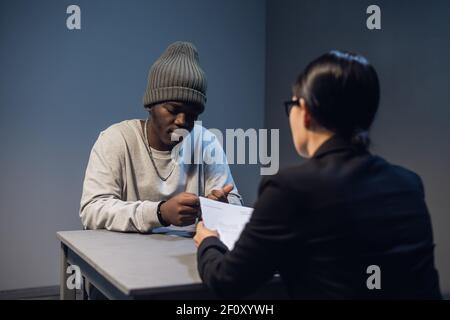Ein Anwalt Mädchen mit Brille und ein junger schwarzer Kerl Kommuniziert im Verhörraum über das Gelände für seine Inhaftierung Stockfoto