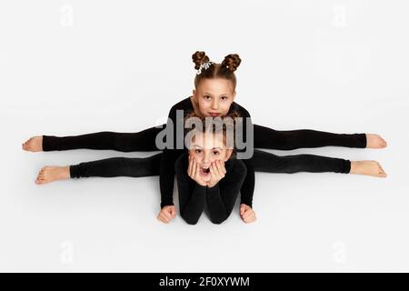 Zwei kleine Mädchen in schwarzer Sportkleidung sitzen auf einer Quergarn. Gute Dehnung und Gymnastik Stockfoto