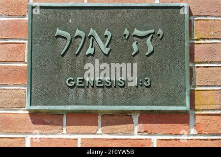 Strukturierte Bronzetafel, die an einer roten Ziegelwand mit hängt Der hebräische Text für 'Es werde Licht' und Genesis 1:3 Uhr Stockfoto
