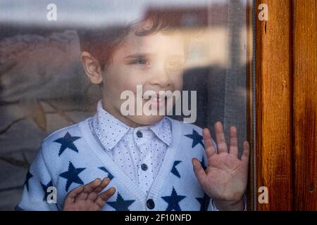 Netter kleiner Junge, der von innen durch das Fenster schaut Stockfoto